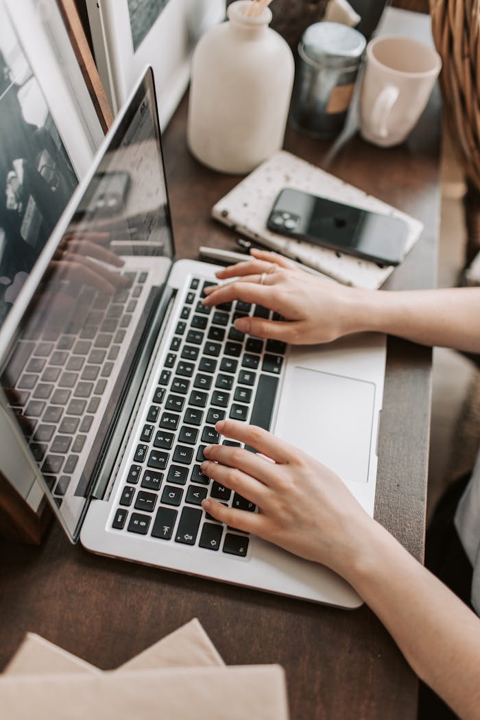 Início From above of unrecognizable woman sitting at table and typing on keyboard of computer during remote work in modern workspace